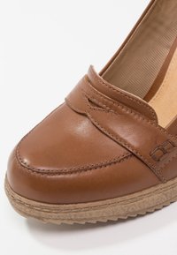 Chaussure en cuir marron à enfiler avec détails de couture, panneau latéral élastique et semelle en caoutchouc texturée pour un usage décontracté.