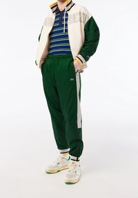 Chándal verde con chaqueta crema que presenta un patrón de cuadros, combinado con un polo a rayas azules y zapatillas blancas con detalles verdes.