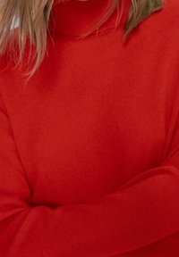 Pull en tricot rouge avec un col haut et des manches longues, présentant des poignets côtelés et une texture lisse.