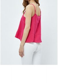 Fuchsia ärmlös topp med en strukturerad design, som har justerbara axelband och en lös passform, kombinerad med vita tajta byxor.