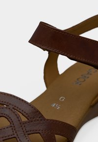 Καφέ δερμάτινο σανδάλι με σχεδιασμό σταυρωτού, ρυθμιζόμενο λουράκι, επίπεδη σόλα και επένδυση με μαλακή επένδυση. Μέγεθος σημειωμένο στο εσωτερικό ως G 4½.