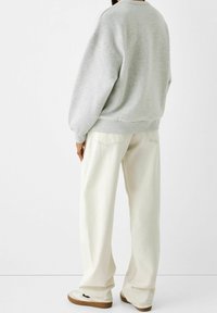 Grey sweatshirt with dropped shoulders, paired with off-white wide-leg pants. Footwear features a light upper with brown sole accents.