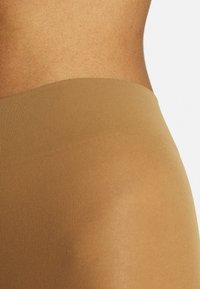 Beige High-Waist-Leggings mit geripptem Muster, glatter Oberfläche und tailliertem Design, das knapp unterhalb der Taille endet.