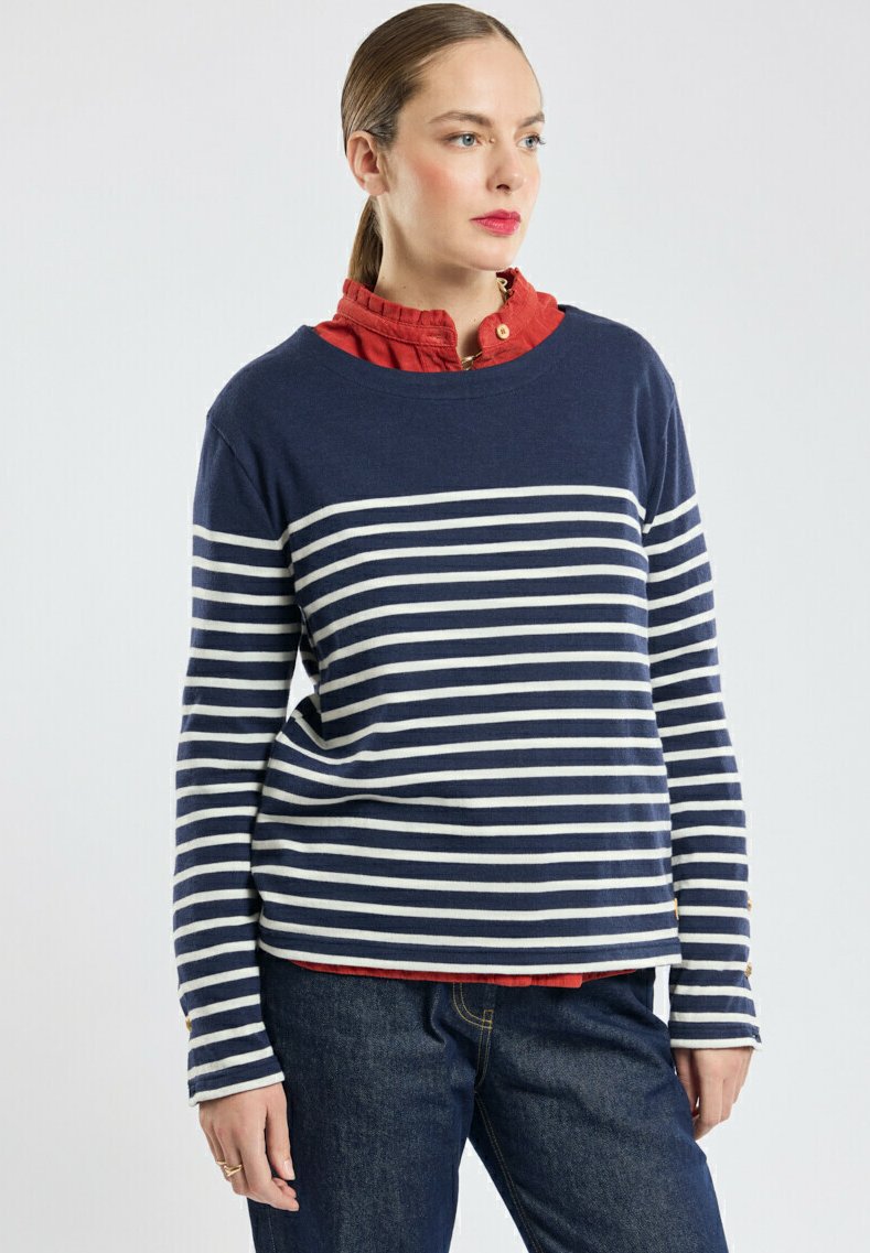 Haut à manches longues rayé bleu marine et blanc, superposé sur une chemise rouge à col, avec un col rond et des accents de boutons dorés sur les manches.