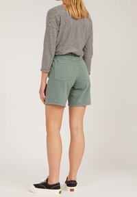 Green cotton shorts with a relaxed fit, two back pockets, and a medium-rise waist. Paired with a black and white striped long-sleeve top and sneakers.