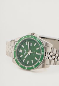 Ceas cu cuarț, cu un cadran și o bezel verde, curea din oțel inoxidabil argintie, marcaje îndrăznețe și afișaj de dată la ora 3.