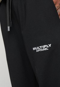 Sorte sweatpants lavet af blødt stof, med en elastisk talje og snoretræk samt en hvid broderet "MULTIPLY APPAREL" logo på siden.