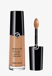 Concealer Luminous Silk Perfect Glow in una bottiglia di vetro con un tappo nero. Presenta un applicatore a spugna, una consistenza liscia e una tonalità beige caldo.
