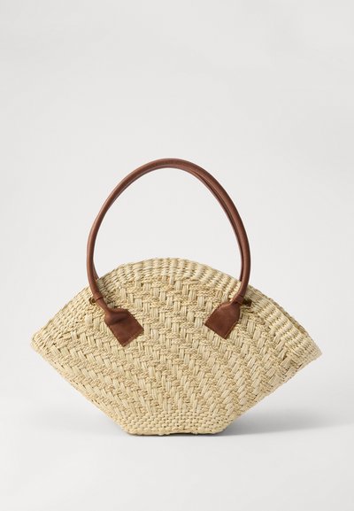 Sac en paille tissée en forme de éventail asymétrique avec des accents et des poignées en cuir brun. Présente une texture naturelle et une couleur beige clair.