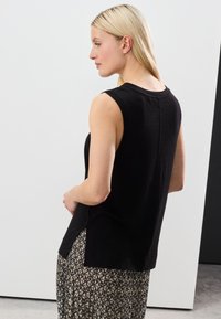 Top noir sans manches à coupe décontractée, texture douce, encolure arrondie et fentes latérales. Associé à une jupe à motifs pour créer un contraste.