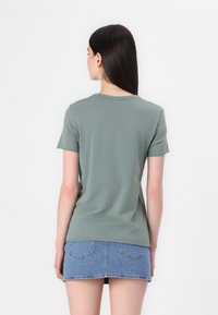 Zelené bavlněné tričko s krátkým rukávem a kulatým výstřihem, kombinované s džínsovou mini sukní. Hladká textura, ležérní design a jednoduchý střih.