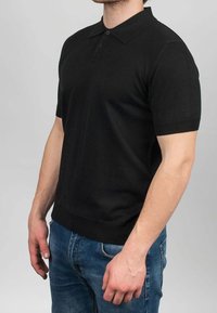 Polo nera a maniche corte con colletto classico, realizzata in tessuto a maglia liscia, caratterizzata da due bottoni e una fascia aderente in vita.