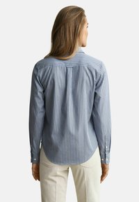 Gestreiftes Hemd mit Knöpfen in Blau und Weiß mit dezenten roten Akzenten, mit abgerundetem Saum und einer Falte am Rücken für mehr Bewegungsfreiheit.