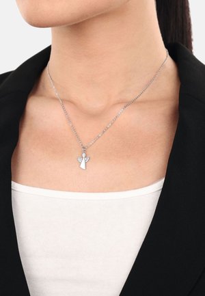 Collarín de ángel de plata con pequeños acentos de piedras claras, unido a una delicada cadena, descansando sobre un blazer negro y una blusa blanca.
