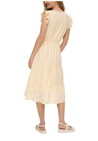 Gestreiftes Midikleid in hellgelb mit Rüschensäumen und einem gestuften Design. Getragen mit hellen Sandalen, die über verstellbare Riemen verfügen.