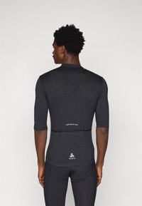 Črno športno dolgi rokav majica z teksturiranim hrbtom, slim fit in odsevnim logotipom na zadnjem robu, zasnovana za zmogljive aktivnosti.