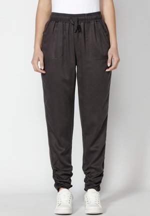 Pantaloni de jogger gri închis cu un talie elastică, șnur și două buzunare laterale. Cureaua elastică la glezne, asortați cu adidași albi.