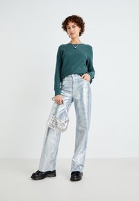 Zelený pletený svetr, lesklé stříbrné kalhoty širokého střihu, černé platformové boty a metallic stříbrná kabelka s ozdobami.