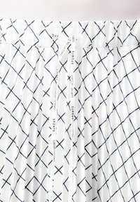 Jupe plissée blanche avec un motif à carreaux diagonaux bleu marine, taille élastique et cordon de serrage avec le texte "SPORTS". Tissu léger.