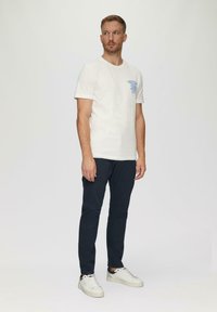 Witte katoenen t-shirt met een blauwe grafische print op de linkerkant van de borst, gecombineerd met een marineblauwe broek en witte sneakers. Eenvoudig, casual ontwerp.
