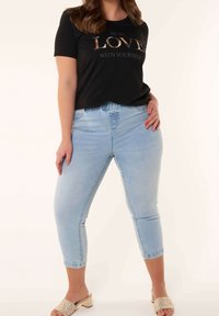 T-shirt noir à manches courtes avec un texte argenté, associé à un jean court bleu clair et des chaussures à enfiler en osier beiges. Ensemble simple et décontracté.