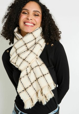 Bufanda crema con un patrón a cuadros en negro, con bordes con flecos. Hecha de una tela texturizada, envuelta de manera casual alrededor del cuello del modelo.