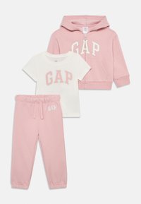 Ensemble pour tout-petit en trois pièces comprenant un sweat à capuche rose zippé, un t-shirt blanc avec le logo "GAP" en rose et un pantalon de jogging assorti en rose avec des poignets élastiques.