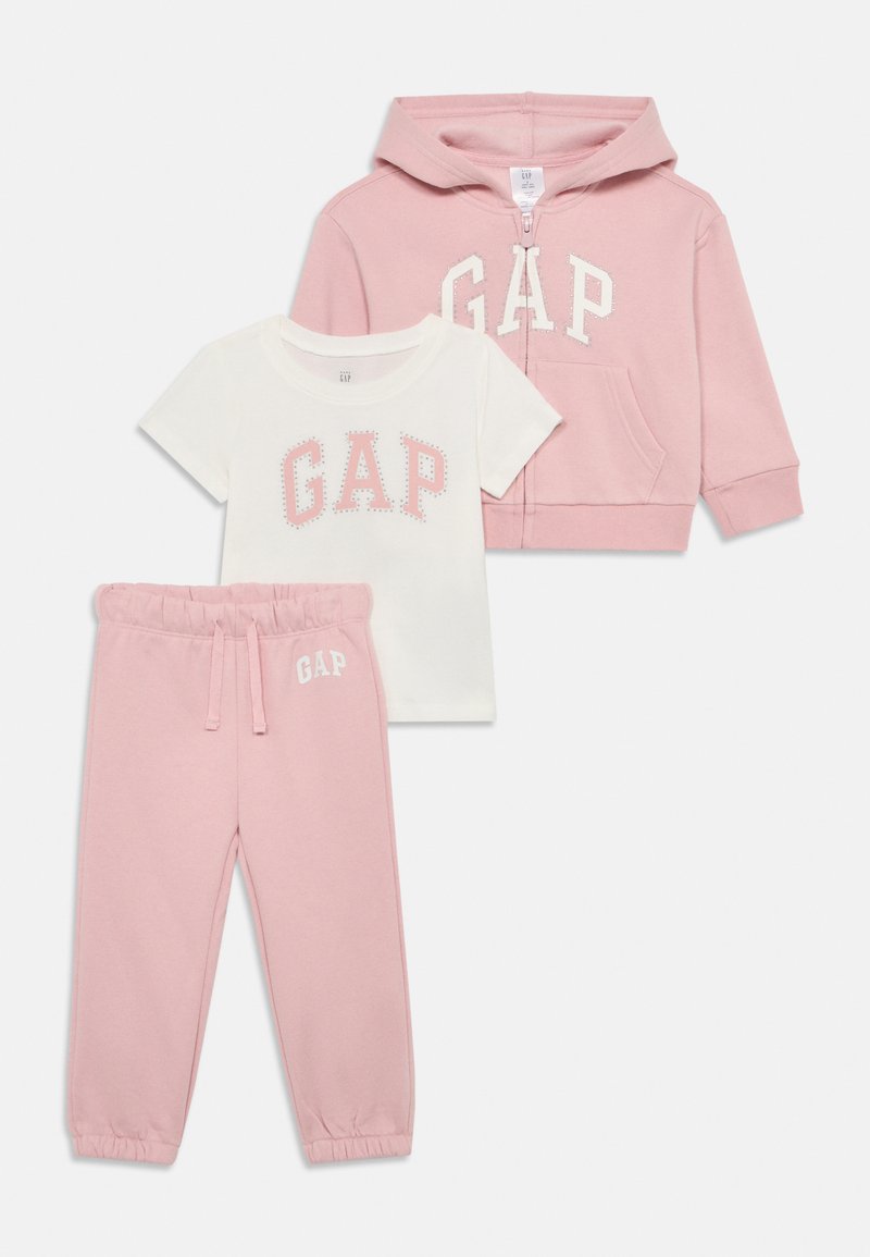 Ensemble pour tout-petit en trois pièces comprenant un sweat à capuche rose zippé, un t-shirt blanc avec le logo "GAP" en rose et un pantalon de jogging assorti en rose avec des poignets élastiques.