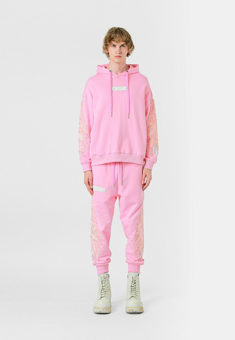 Juego de sudadera y pantalones de chándal rosa, hecho de una tela suave, con diseños de alas bordadas en las mangas y en los pantalones, y detalles de hardware metálico.