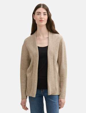 Beige cardigan met een losse fit, gemaakt van textiel met textuur. Open voorkant ontwerp, lange mouwen, en gedragen over een zwart topje en jeans.