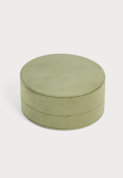 Boîte à bijoux ronde recouverte de suède vert clair avec un couvercle, présentée sur un fond clair uni.