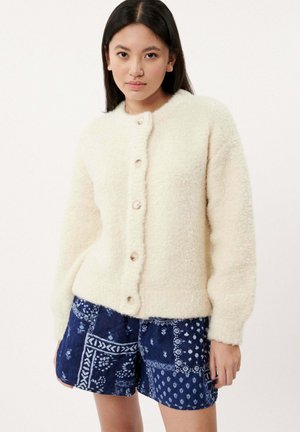 Cremfarbener, flauschiger Strickcardigan mit rundem Kragen und sechs Knopfverschlüssen, kombiniert mit gemusterten blauen Shorts mit weißen Designs.