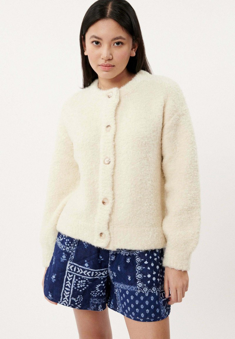 Crème-kleurige furry gebreide cardigan met ronde kraag en zes knoopsluitingen, gecombineerd met gestreepte blauwe shorts met witte patronen.