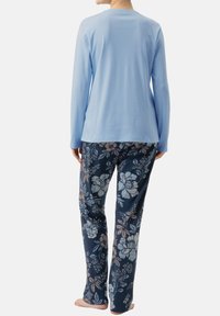 Vaaleansininen pitkähihaine paita yhdistettynä tummansinisiin kukkakuosisempiin housuihin, joissa on suuria kukkia ja lehtiä pehmeissä vaaleanpunaisissa, beigen värisissä ja sinisissä sävyissä.