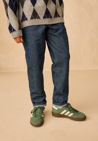Szary i granatowy sweter w wzór argyle, ciemnoniebieskie dżinsy oraz zielone zamszowe trampki z białymi paskami i brązowymi podeszwami.