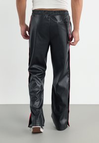 Pantaloni din piele neagră cu un finisaj lucios, având dungi laterale roșii și talie cu snur, tăiați larg la glezne, cu o textură netedă.