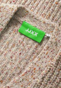 Gruba, dzianinowa sweter w odcieniu beżu z wielokolorowymi kropkami. Posiada zieloną metkę z napisem "JJXX" w białym kolorze oraz oznaczeniem rozmiaru "S". Teksturowana tkanina.