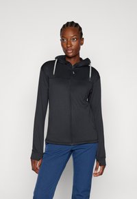 Sudadera negra con cremallera y un patrón texturizado, que cuenta con capucha ajustable y mangas largas. Llevada sobre pantalones azules, mostrando un diseño elegante.