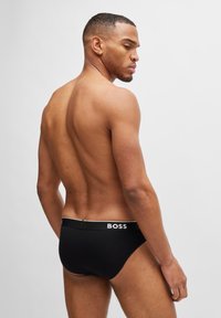 Black cotton brief with a soft waistband featuring white "BOSS" logo. Minimalistic design, snug fit, smooth texture.