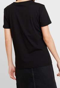 Camiseta de algodón negra con mangas cortas y cuello redondo, que presenta un corte holgado y una textura suave. Detalle de costura sutil en el dobladillo.
