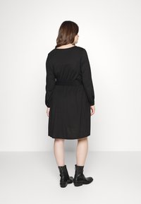 Vestido preto de mangas longas com cintura ajustada e saia rodada. As costas apresentam um decote redondo e textura suave, combinado com botas de tornozelo.