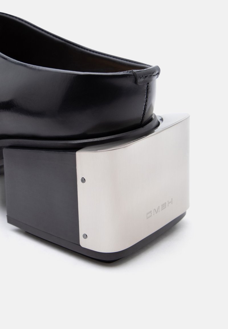 Black leather shoe with a high square block heel featuring a reflective silver metal plate on the back with embossed text.