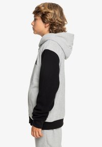 Grijze zip-up hoodie met zwarte mouwen, verstelbare capuchon en geribde manchetten. Heeft een eenvoudig ontwerp en een zachte textuur die geschikt is voor casual draag.