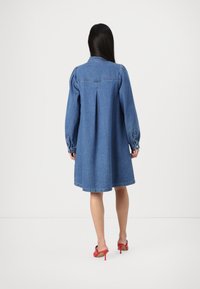 Light blue denim dress with long puff sleeves, a buttoned collar, and a pleat at the back. Finished with a flared hemline and cuff buttons.