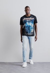 Musta graafinen t-paita, jossa on sinistä ja valkoista painatusta, yhdistettynä vaaleansinisiin farkkuihin ja valkoisiin lenkkareihin. Yksinkertainen muotoilu, istuva siluetti.