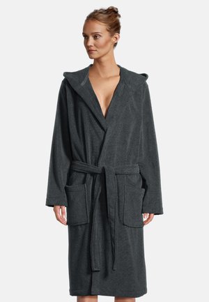 Kobieta ubrana w ciemnoszary szlafrok z kapturem, paskiem i dużymi przednimi kieszeniami, stojąca na tle jednolitego jasnego tła.