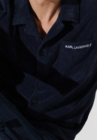 Námořnická modrá košele na knoflíky vyrobená z měkké tkaniny, s náprsní kapsou, na které je bíle vyšitý nápis "KARL LAGERFELD".