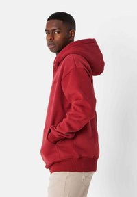 Sudadera de forro polar roja con un bolsillo canguro, puños acanalados y capucha con cordón. Textura suave con costuras visibles y acentos de botón.
