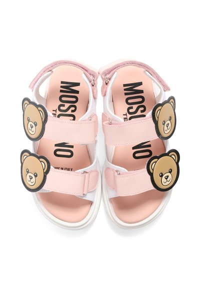 Różowe sandały dziecięce z dwoma regulowanymi paskami, z których każdy ozdobiony jest uśmiechniętą twarzą misia, oraz logo "Moschino" na wkładce.