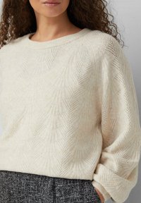 Jasna kremowa sweter o textured wzorze z subtelnym diamentowym motywem. Rękawy są lekko oversize, co zwiększa komfort noszenia.